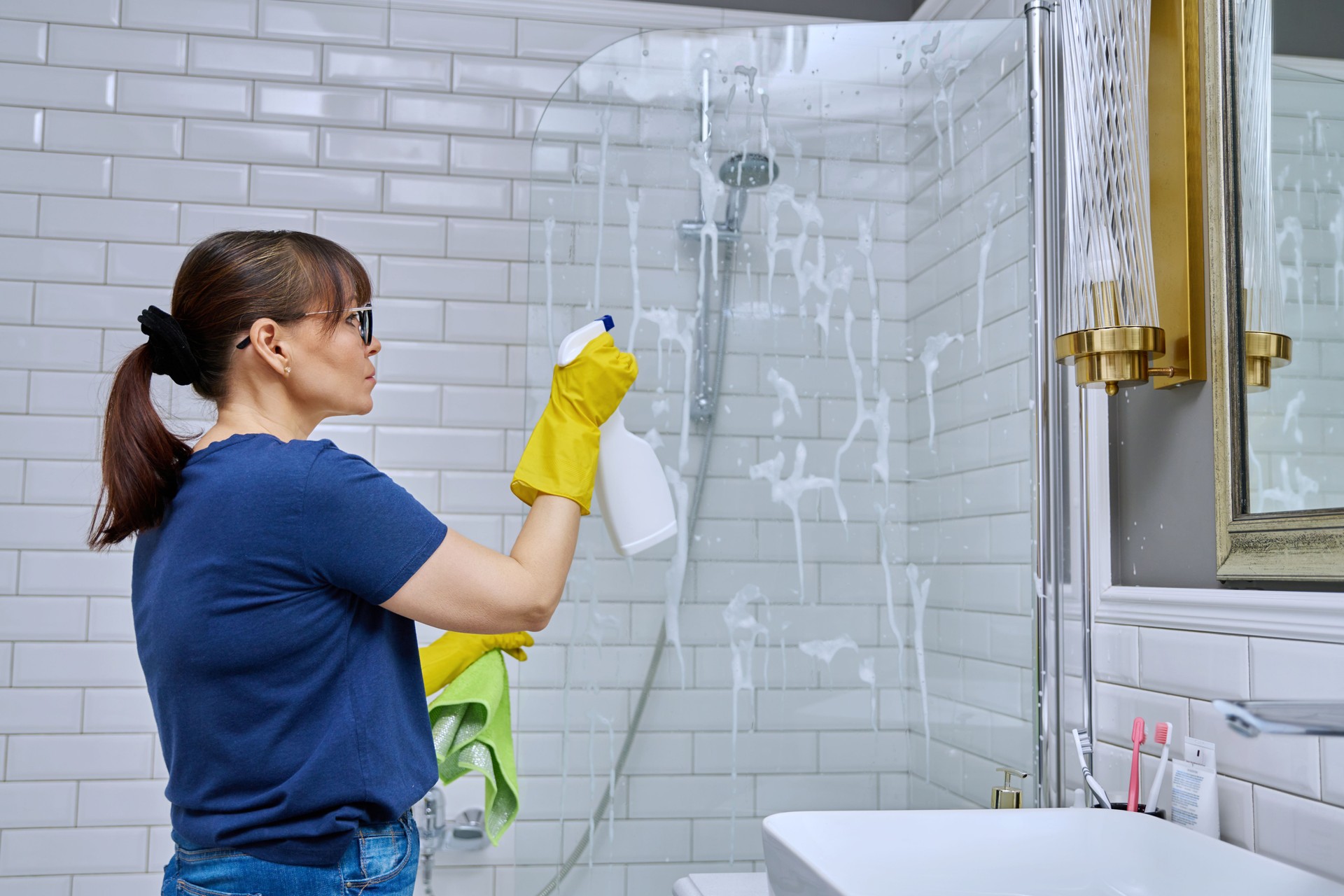 Woman cleaning bathroom, washing glass in shower